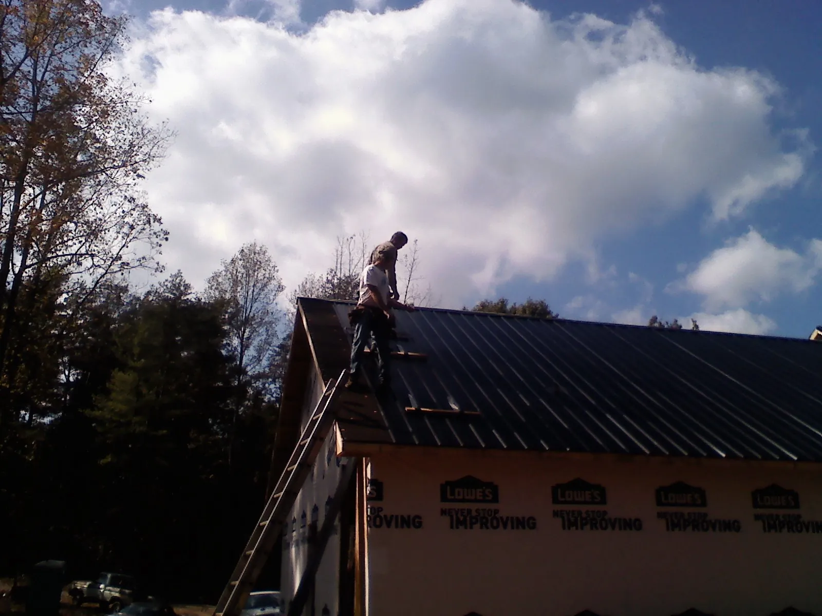 Roofer fastening dark metal panels high against a cloudy sky, from a Roof Inspection job in Quincy